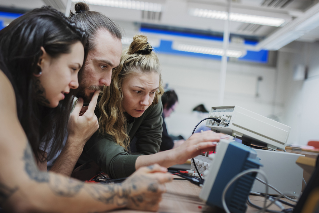 Tre studerande, två kvinnor och en man, arbetar koncentrerat med elektronik.