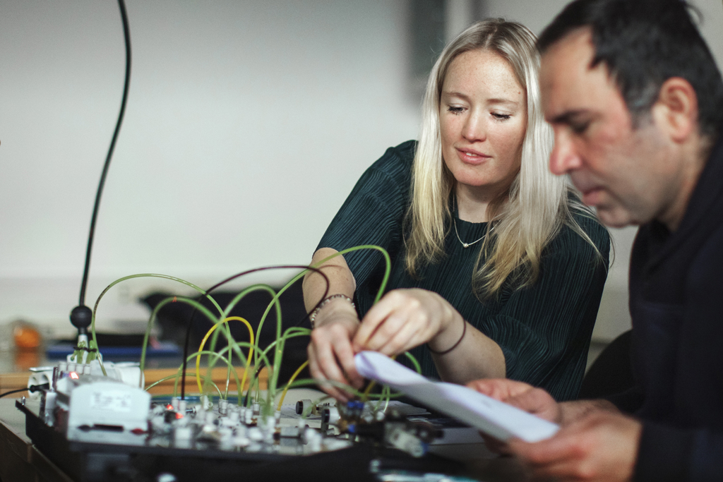 Två studerande, en kvinna och en man, arbetar med sladdar och elektronik.