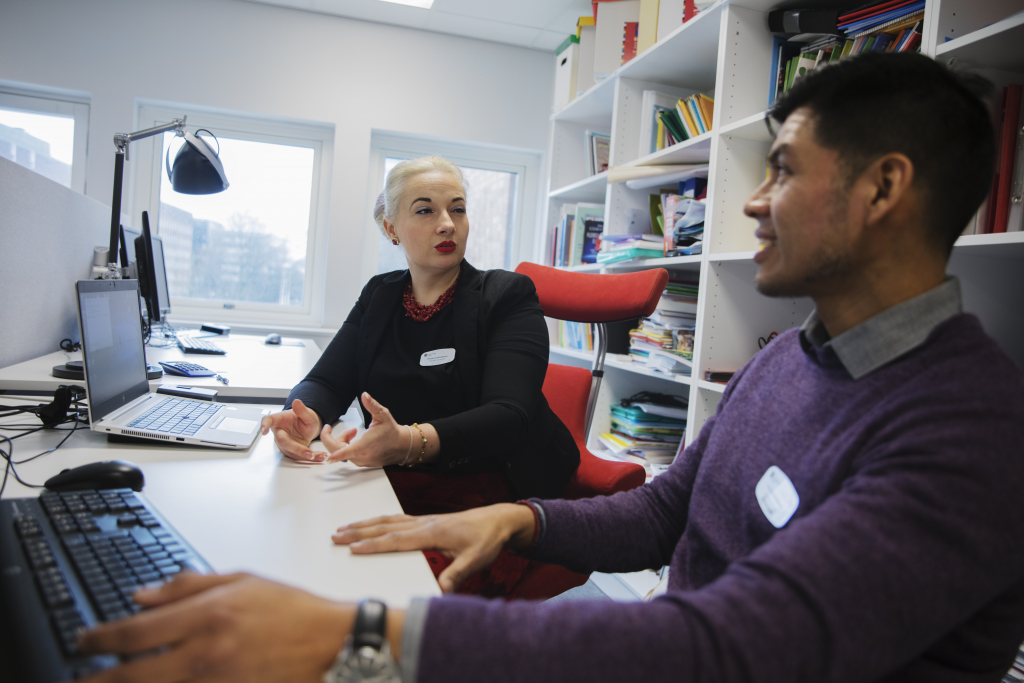 En man och en kvinna sitter framför datorn. De tittar på varandra och ser ut att diskutera något.
