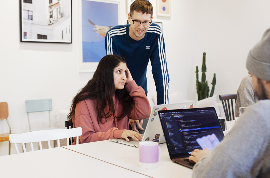 Tre personer sitter vid ett bord på en arbetsplats och arbetar med programmering.