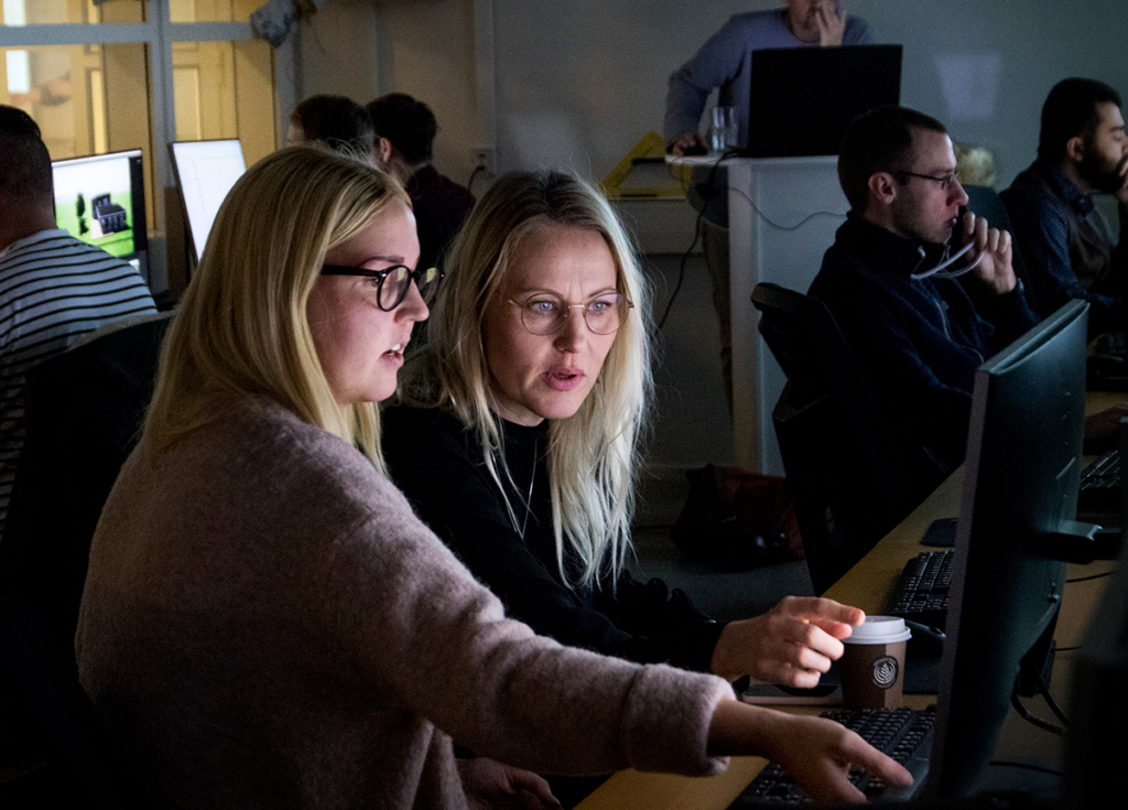 Två kvinnor sitter framför en datorskärm och pratar med varandra.